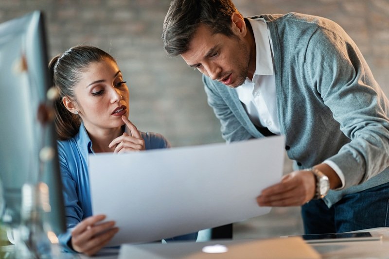 Two entrepreneurs cooperating while reading blueprints and working together in the office.